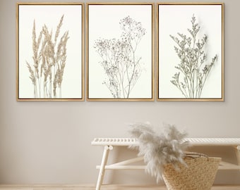 May include: Three framed prints of dried botanicals, featuring a cluster of dried grasses, a delicate sprig of dried flowers, and a bunch of dried ferns. The prints are displayed on a white wall above a white wooden bench with a woven basket.