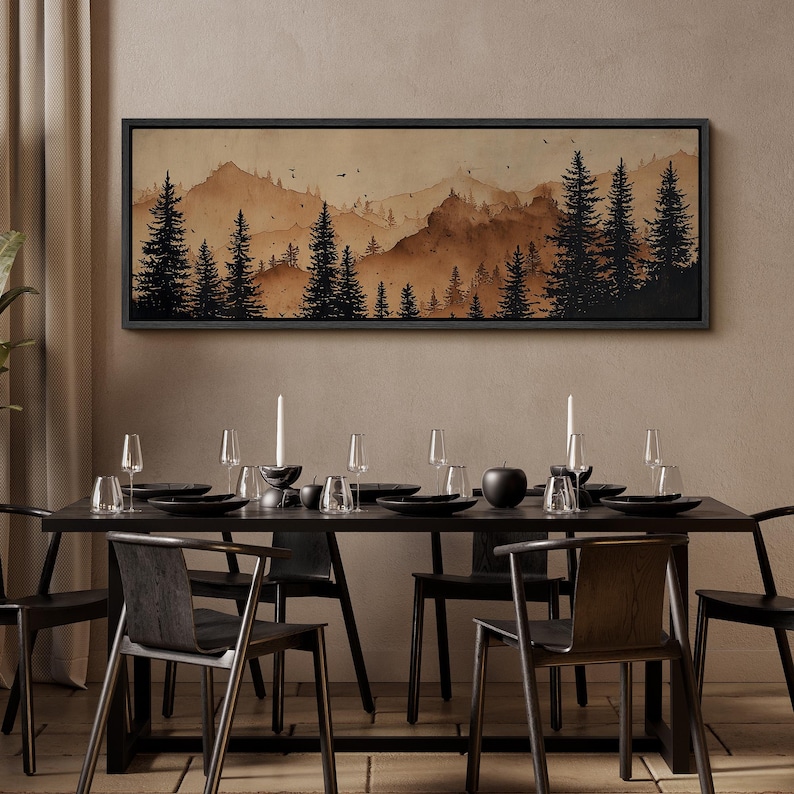 May include: A dining room scene featuring a long, black table set for a meal. Above the table hangs a framed landscape painting of a mountain range and pine trees in shades of brown. The table is set with black plates, glasses, and candles.