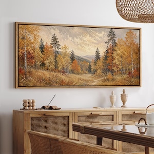May include: A rectangular landscape painting in a wooden frame depicting a forest scene during autumn. The artwork features tall evergreen and deciduous trees with golden, orange, and brown foliage set against a backdrop of distant mountains.