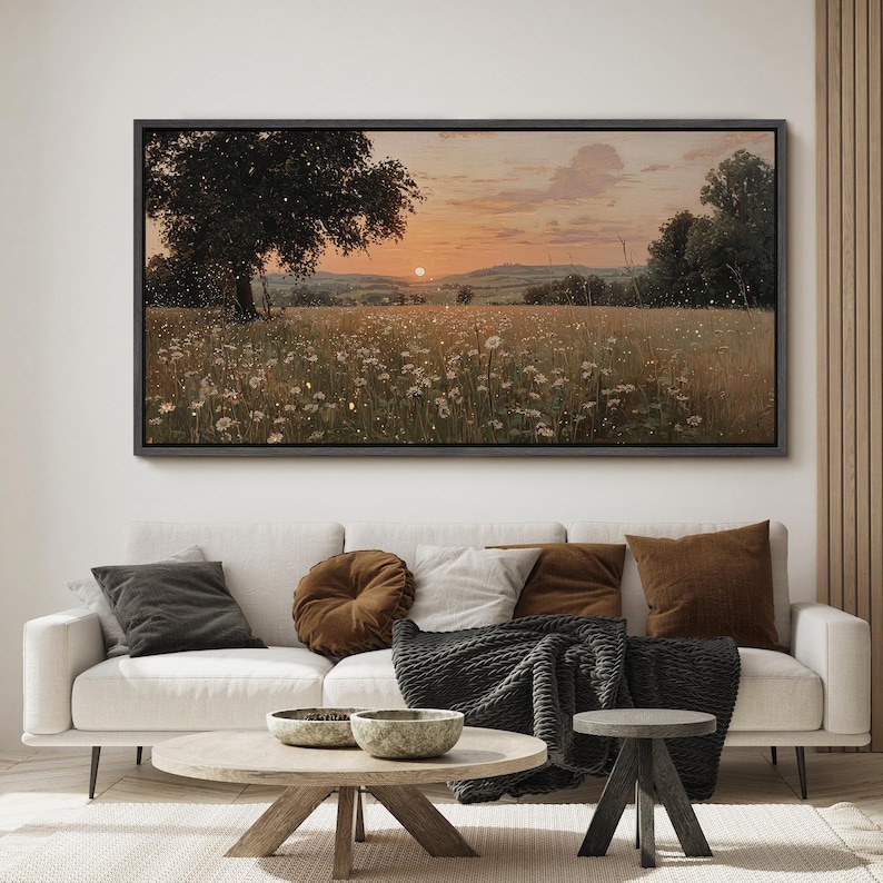 Puede incluir: Un cuadro de paisaje rectangular en un marco oscuro que representa una puesta de sol sobre un campo de flores silvestres blancas y hierba alta. Un gran &aacute;rbol se alza a la izquierda, mientras el horizonte muestra colinas bajo un cielo anaranjado.