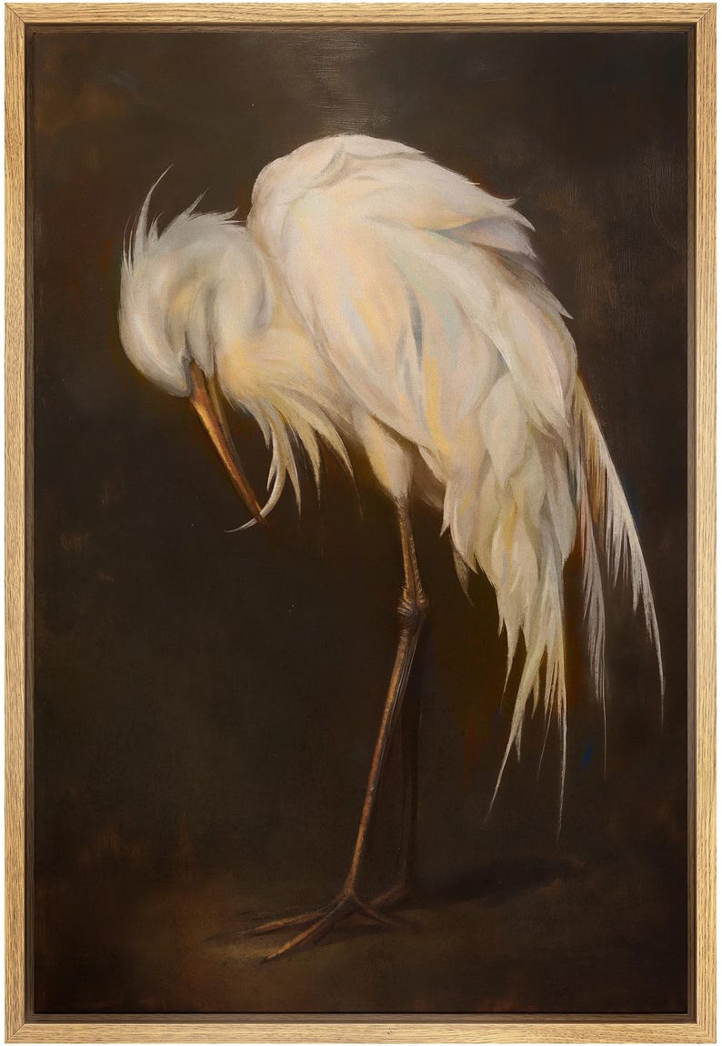 May include: A framed painting of a white egret with its head tucked down, showcasing its long beak and delicate feathers. The bird's legs are thin and brown, set against a dark brown background. The artwork is in a wooden frame.