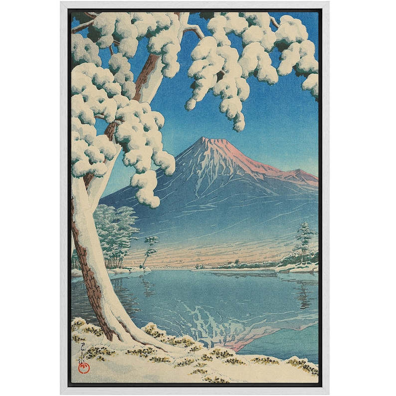 Puede incluir: Una estampa en madera que representa el monte Fuji en la distancia, cubierto de nieve. Un gran &aacute;rbol con ramas cubiertas de nieve se encuentra en primer plano, con un lago en el plano intermedio. La estampa est&aacute; enmarcada en un marco blanco.