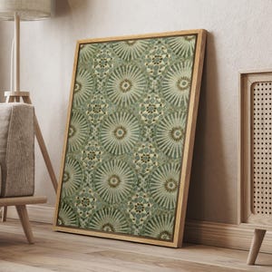 May include: A framed artwork featuring a repeating pattern of stylized, radial designs in shades of green and beige. The artwork is displayed in a light-colored wooden frame, leaning against a wall. The pattern has a mosaic-like appearance.