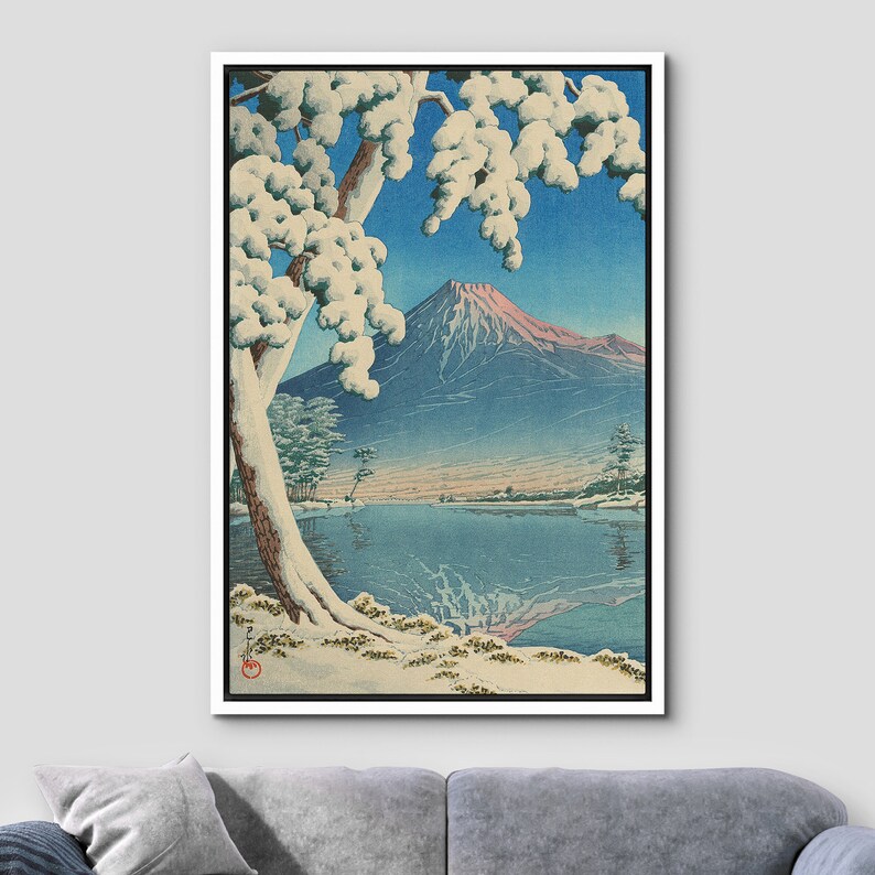 Puede incluir: Una estampa japonesa tradicional en madera que representa el monte Fuji en la distancia, con un &aacute;rbol cubierto de nieve en primer plano y un lago tranquilo que refleja la monta&ntilde;a. El cielo es de un azul vibrante, y la monta&ntilde;a es de un rosa y un azul suaves.