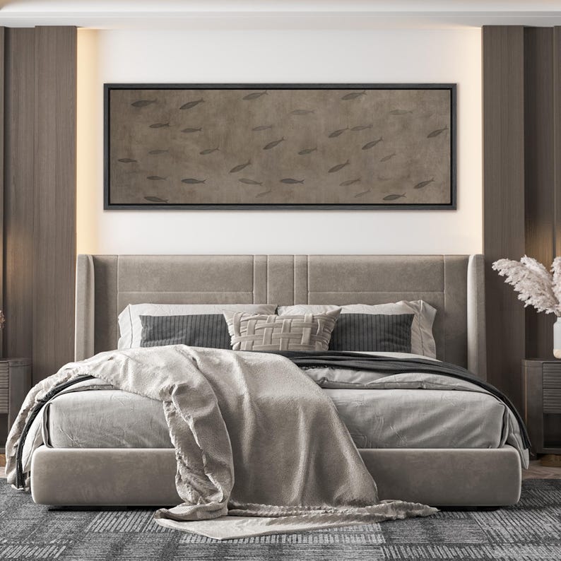 Puede incluir: Escena de dormitorio con una cama grande, un cabecero tapizado gris y ropa de cama. Encima de la cama hay una obra de arte rectangular enmarcada con un patr&oacute;n de siluetas de peces. La habitaci&oacute;n tiene una paleta de colores neutros con detalles en madera y una alfombra estampada.