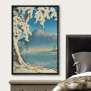 Puede incluir: Una estampa en madera del monte Fuji en invierno. La monta&ntilde;a est&aacute; en el fondo, con un &aacute;rbol cubierto de nieve en primer plano. Un lago est&aacute; en el medio, con nieve en el suelo y hielo en el agua.