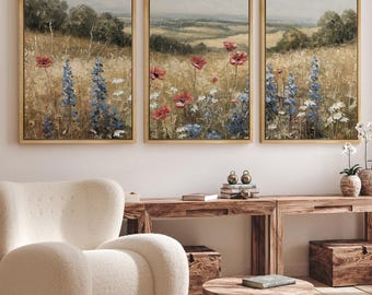Puede incluir: Tres pinturas de paisaje enmarcadas que representan un campo de flores silvestres en tonos rojos, azules y blancos. La obra de arte presenta un marco dorado y una paleta de colores neutros, adecuada para la decoración del hogar. Las pinturas se exhiben sobre una consola de madera.