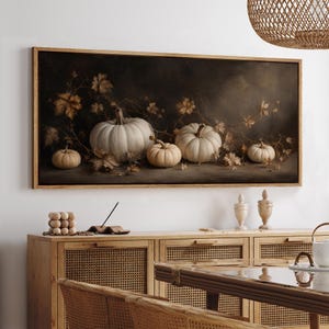May include: A rectangular wall art print featuring a dark, moody still life painting of four white pumpkins of varying sizes arranged with scattered dried autumn leaves and thin, winding vines against a deep, shadowed background.
