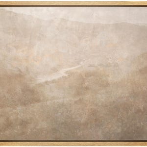 May include: A framed landscape art print featuring a muted color palette of beige, tan, and brown. The artwork depicts a mountainous terrain with a river winding through the valley. The frame is made of light-colored wood.