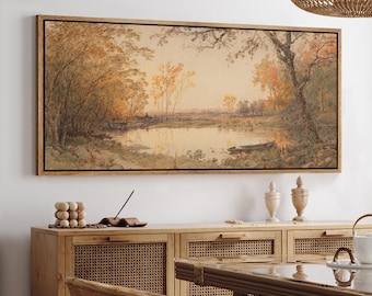 May include: A framed landscape painting depicts a serene waterscape with trees in autumn colors. The artwork features a wooden frame and is displayed above a wooden cabinet. The scene includes a boat on the water, with warm tones dominating the color palette.