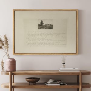 May include: A framed artwork featuring a sepia-toned landscape sketch above handwritten script. The artwork is encased in a light brown wooden frame. The landscape sketch depicts a tree and buildings. The script is in a cursive font.