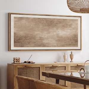 May include: A framed artwork with a light brown background and handwritten text. The artwork is in a wooden frame and hangs above a wooden cabinet with woven panels. Decorative items are on the cabinet.