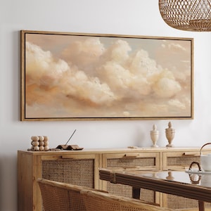 May include: A framed canvas art piece featuring a soft, impressionistic painting of fluffy, peach-colored clouds against a pale blue sky. The artwork is encased in a natural wood frame, adding a touch of warmth to the serene scene.