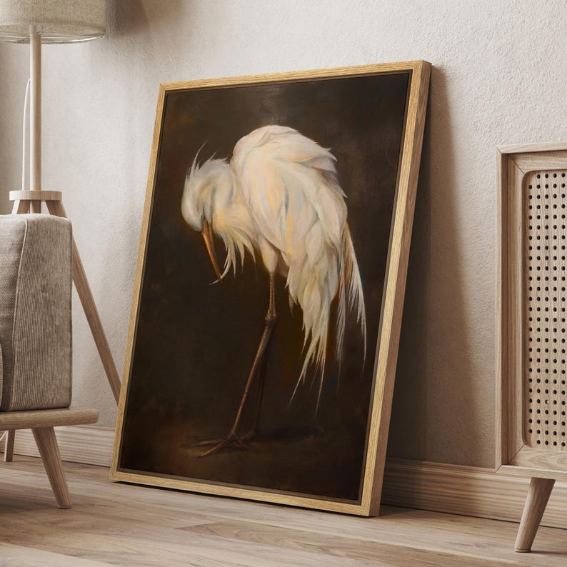 May include: A framed artwork shows a white egret with its head lowered, set against a dark brown backdrop. The bird's feathers are detailed with soft, light colours. The frame is made of light-coloured wood.