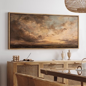 May include: A framed landscape painting depicts a dramatic sky filled with swirling clouds in shades of brown, gold, and blue. The artwork is displayed above a wooden cabinet with woven cane doors, creating a warm, inviting atmosphere.