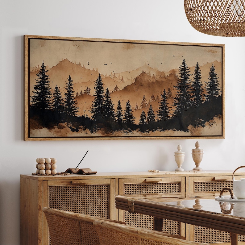 May include: A framed landscape art print featuring a watercolor-style forest scene in shades of brown and black. The artwork depicts silhouetted pine trees in the foreground with mountains in the background. The frame is made of light-colored wood.
