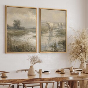 May include: Two framed wall art prints featuring a landscape scene with a river and horses. The left print shows a grassy field with a tree and a river. The right print depicts three horses walking through shallow water in a muted, neutral color palette.