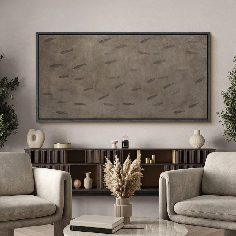 Puede incluir: Obra de arte rectangular enmarcada que representa un grupo de peces sobre un fondo marr&oacute;n. El lienzo con marco negro cuelga sobre un mueble de madera oscura y dos sillones beige. Ideal para el sal&oacute;n.