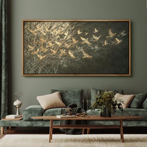 May include: A framed artwork depicts a flock of golden birds in flight against a dark, textured background. The birds are detailed with outstretched wings, set against a backdrop of bare tree branches. The frame is a warm, natural wood tone.
