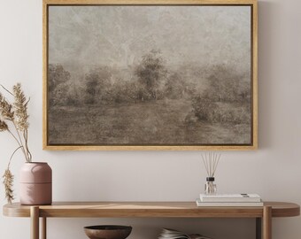 May include: A framed landscape art print with a muted color palette of brown and gray tones. The artwork depicts a hazy, indistinct scene of trees and a field. The frame is a light brown color, and the artwork is displayed on a wooden console table.