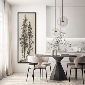 May include: A framed black and white print of two tall pine trees. The artwork hangs on a white wall in a modern dining room setting. The room features a round black table, chairs, and pendant lights.
