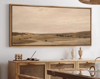 May include: A framed landscape painting depicts a serene, muted-color scene of rolling hills and a vast sky. The artwork, in shades of beige, brown, and gray, evokes a sense of calm. The painting is displayed above a wooden cabinet with woven panels.