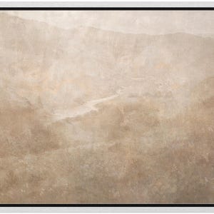 May include: A framed landscape art print featuring a muted color palette of beige, tan, and brown. The artwork depicts a mountain range and a river winding through a valley. The print is encased in a white frame with a black inner border.