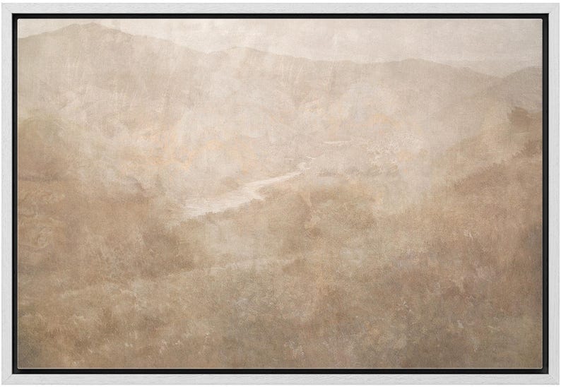 May include: A framed landscape art print featuring a muted color palette of beige, tan, and brown. The artwork depicts a mountain range and a river winding through a valley. The print is encased in a white frame with a black inner border.