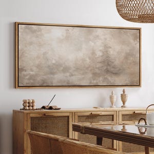 May include: A large rectangular canvas art piece with a light brown and gray abstract design, framed in a light wood. The artwork hangs above a wooden cabinet with woven cane doors and drawers. Decorative items are on the cabinet.