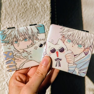 Könnte beinhalten: Zwei Kompaktspiegel mit Anime-Illustrationen. Der erste Spiegel zeigt eine Figur mit weißen Haaren und blauen Augen, die eine weiße Katze mit Sonnenbrille hält. Der zweite Spiegel zeigt eine Figur mit weißen Haaren und blauen Augen, die eine weiße Katze mit Sonnenbrille hält.