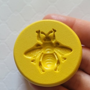 May include: Yellow silicone mold with a bee design. The mold is round and has a textured surface.