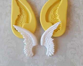 May include: Two yellow silicone molds for making angel wings. The molds are shown with two white angel wings that have been made using the molds.