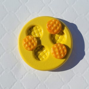 May include: Yellow silicone mold with four round impressions for making waffle-shaped polymer clay earrings. Three orange waffle-shaped polymer clay earrings are shown in the mold.