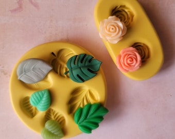 May include: Two silicone molds for making polymer clay jewelry. One mold has two rose shapes, one in pink and one in peach. The other mold has five leaf shapes, one in gray, one in green, and three in different shades of green.