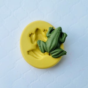 May include: A yellow silicone mould with a detailed frog design. The mould is used for making cake decorations or other edible treats.