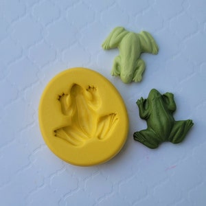 May include: A yellow silicone mould for making frog-shaped decorations. Two green frogs are shown next to the mould.