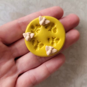 May include: A yellow silicone mold with six bee-shaped cavities. The mold is filled with six small, light pink bee figurines.