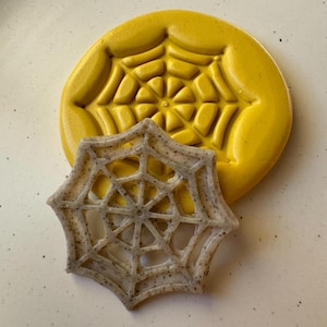 May include: A yellow silicone mold with a spiderweb design and a white plastic spiderweb cookie cutter.