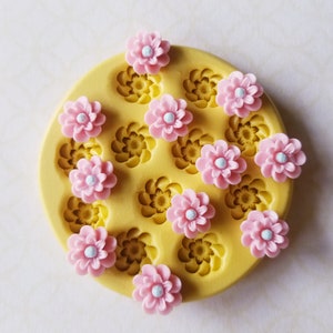 May include: A yellow silicone mold with 10 flower-shaped cavities. The mold is filled with pink and white fondant flowers.