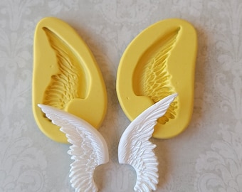 May include: Two yellow silicone molds for making angel wings, with two white angel wings made from the molds.