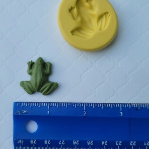 May include: A green frog figurine and a yellow silicone mould of a frog. The mould is about 5 cm in diameter. A blue ruler is in the background.