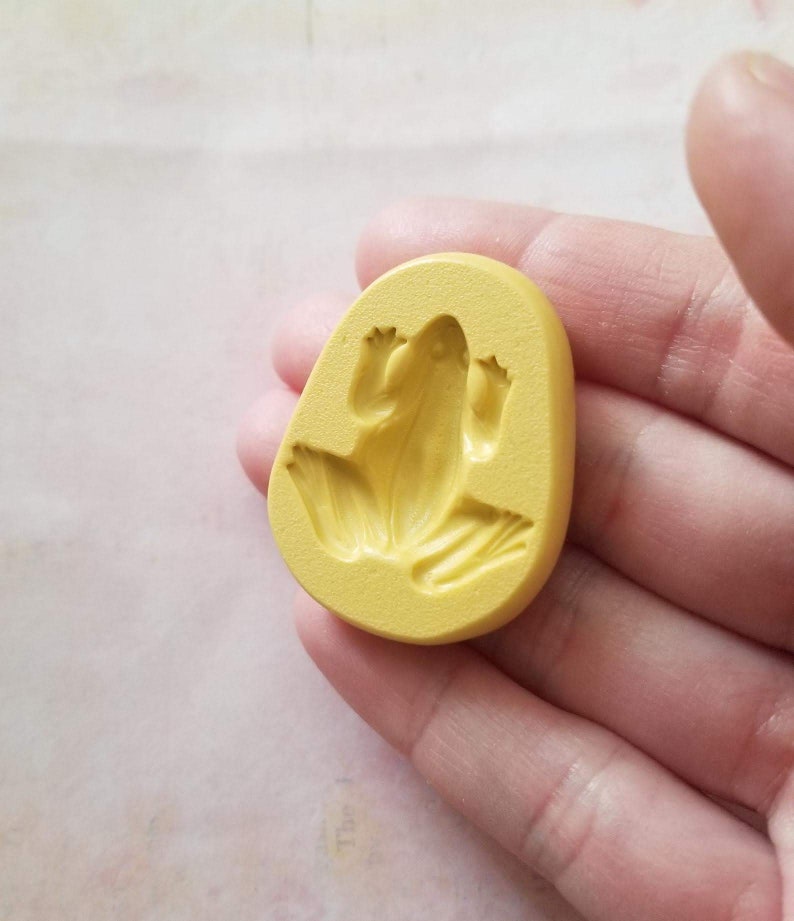 May include: Yellow silicone mould for making a frog-shaped object. The mould is in the shape of a frog with its legs outstretched.