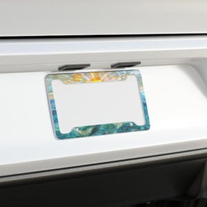 May include: A rectangular license plate frame featuring a stained glass style design. The top section displays a yellow and orange sunburst pattern, while the bottom and sides showcase wavy, overlapping shades of blue, teal, and green glass.