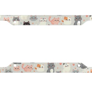 May include: A car number plate frame featuring a repeating pattern of cartoon cats in various colours on a light grey background. The cats have different expressions and small pink hearts.