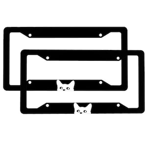 May include: Two black metal license plate frames with a white cat peeking out from behind each frame.