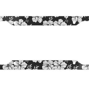 May include: Black license plate frame with a white floral pattern. The frame features a repeating design of hibiscus flowers and leaves against a black background. The frame has a rectangular shape with rounded corners and a hole for mounting.