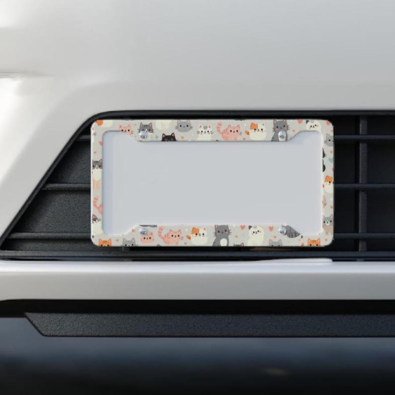 May include: A car license plate frame featuring a repeating pattern of cartoon cats in various colours. The frame has a white border with a grey background.