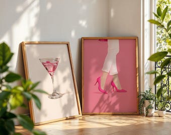 Könnte beinhalten: Zwei gerahmte Kunstdrucke. Einer zeigt einen rosa Cocktail in einem Martiniglas. Der andere zeigt die Beine einer Person in weißer Hose und pinkfarbenen High Heels vor einem rosa Hintergrund. Beide sind in Holzrahmen.