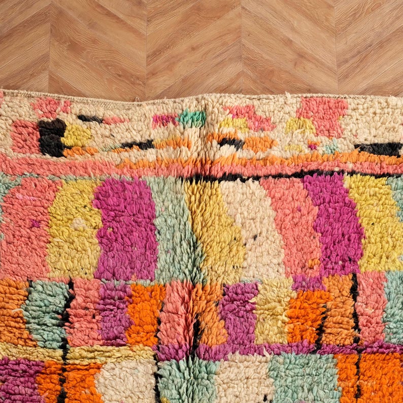 May include: A vibrant, textured rug with a geometric design. The rug showcases a mix of bright colours, including pink, orange, yellow, green, and cream. The pattern is made up of rectangular and square shapes, creating a patchwork effect.