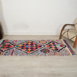 Puede incluir: Una alfombra rectangular multicolor con un patrón geométrico de diamantes. La alfombra presenta una mezcla de tonos azules, rosas, verdes y naranjas. La alfombra mide aproximadamente 60 cm de ancho y 150 cm de largo, con bordes con flecos.